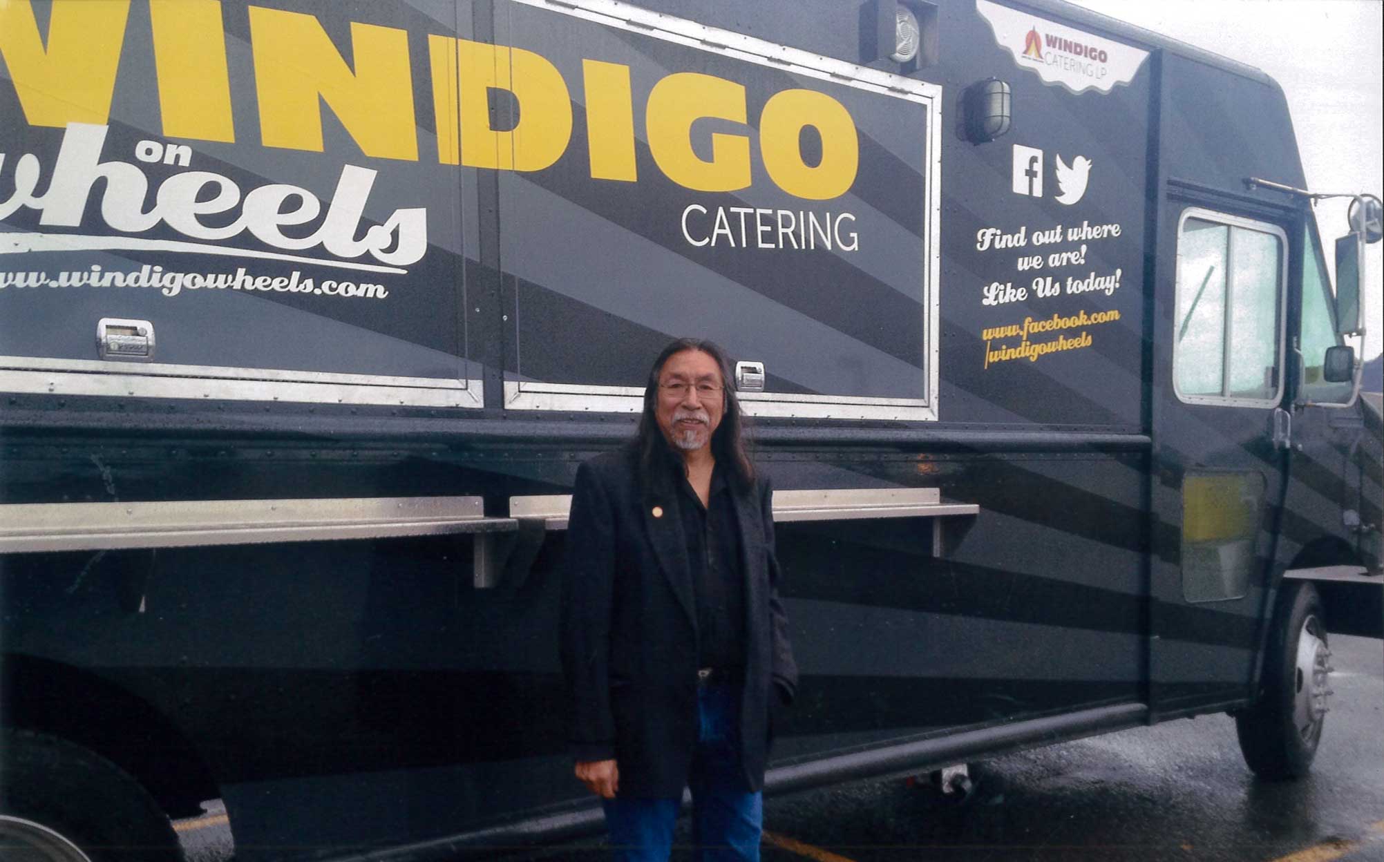 Native man stands in front of a food truck "Windigo Catering on Wheels"