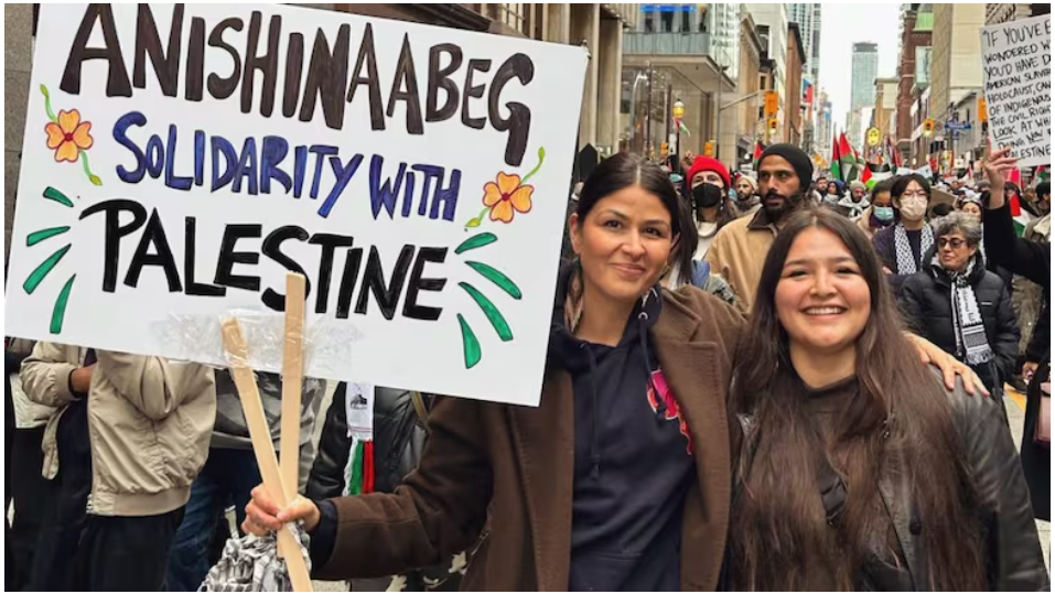 a native woman holds a sign saying "Anishinaabeg solidarity with Palestine" in front of a rally